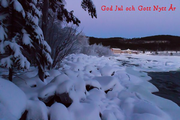 Bild på snötäckt skog, stenar och Storforsen med Hotell Storforsen i bakgrunden och texten God Jul och Gott Nytt År
